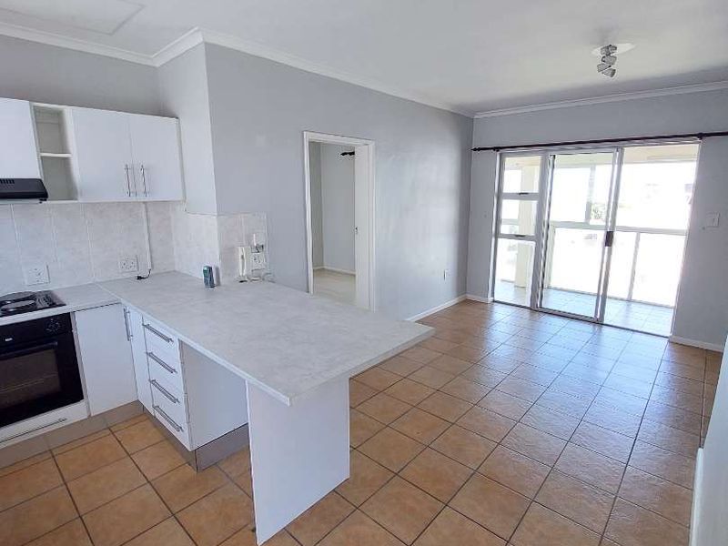 Open-plan kitchen and living area featuring tiled flooring, built-in cabinetry with integrated appliances, and sliding glass doors leading to a balcony.