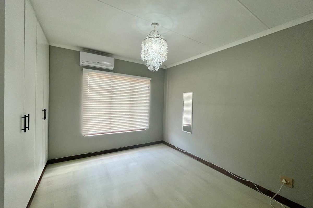A bright and spacious bedroom featuring built-in cupboards, a wall-mounted air conditioning unit, and modern window blinds.