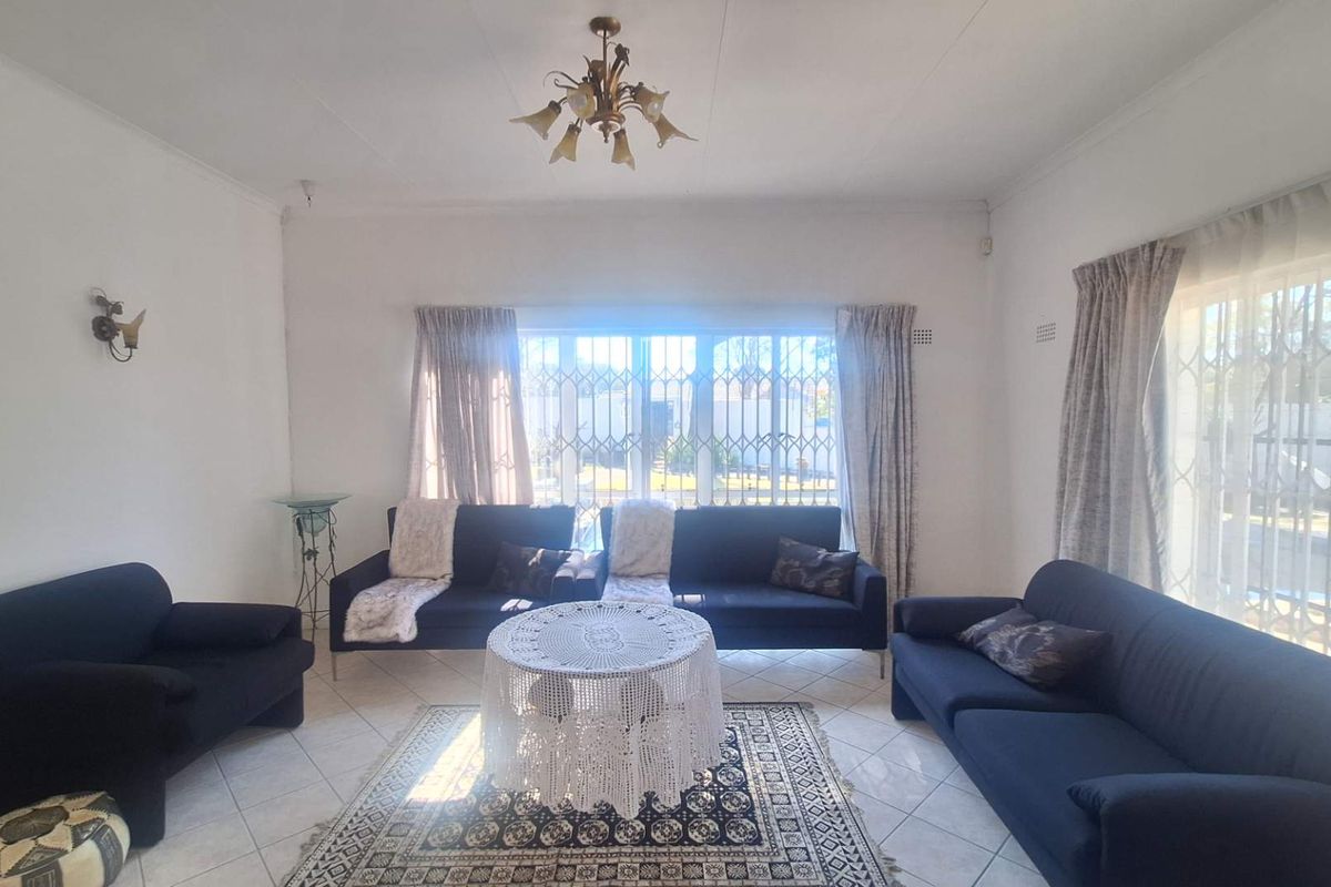 A bright living room featuring tiled flooring, large windows with security gates, and classic lighting fixtures.