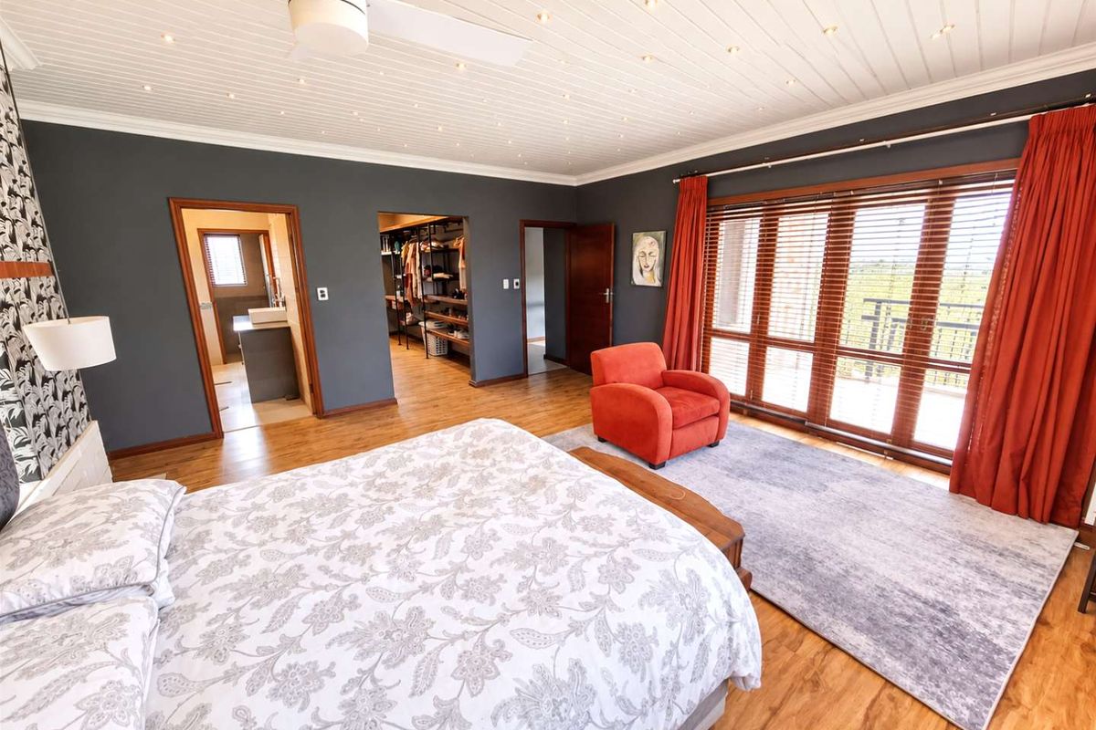 Spacious bedroom featuring timber flooring, a tongue and groove ceiling with recessed lighting, an en-suite bathroom, and a walk-in wardrobe with balcony access.