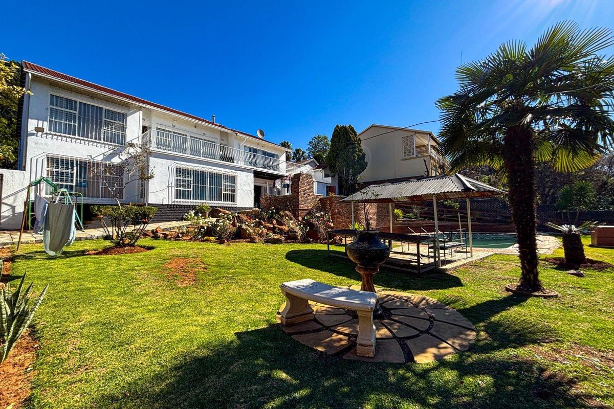 Spacious rear garden featuring a swimming pool, covered patio area, balcony, and established landscaping with a stone bench.