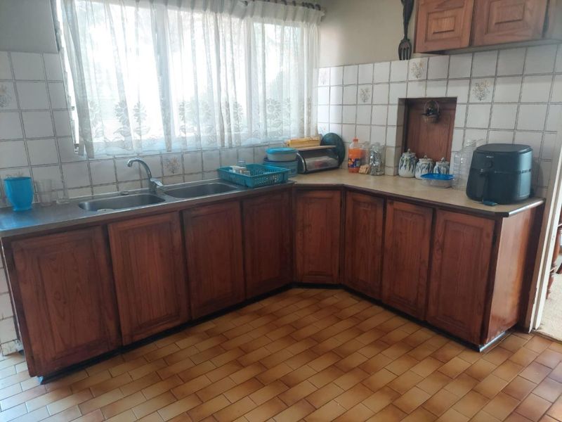 A dated kitchen featuring wooden cabinetry, laminate countertops, double stainless steel sink, and ceramic wall and floor tiling.