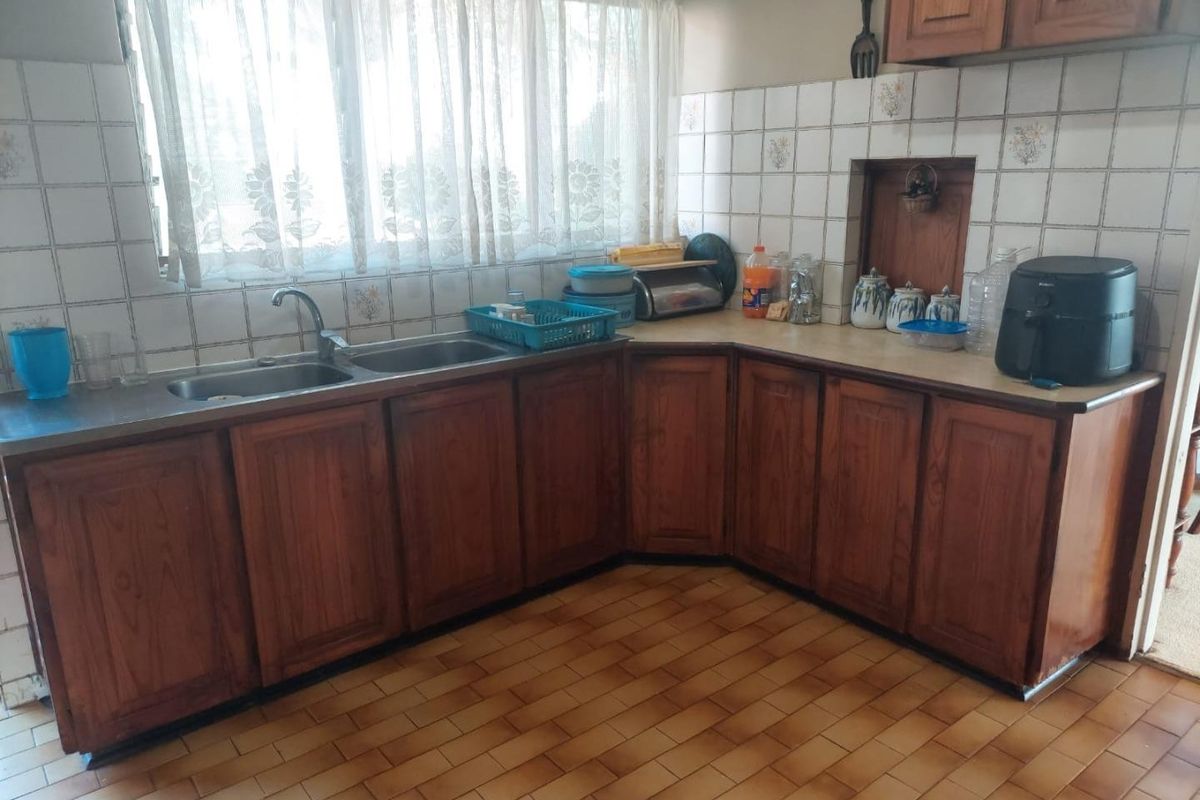 A dated kitchen featuring wooden cabinetry, laminate countertops, double stainless steel sink, and ceramic wall and floor tiling.