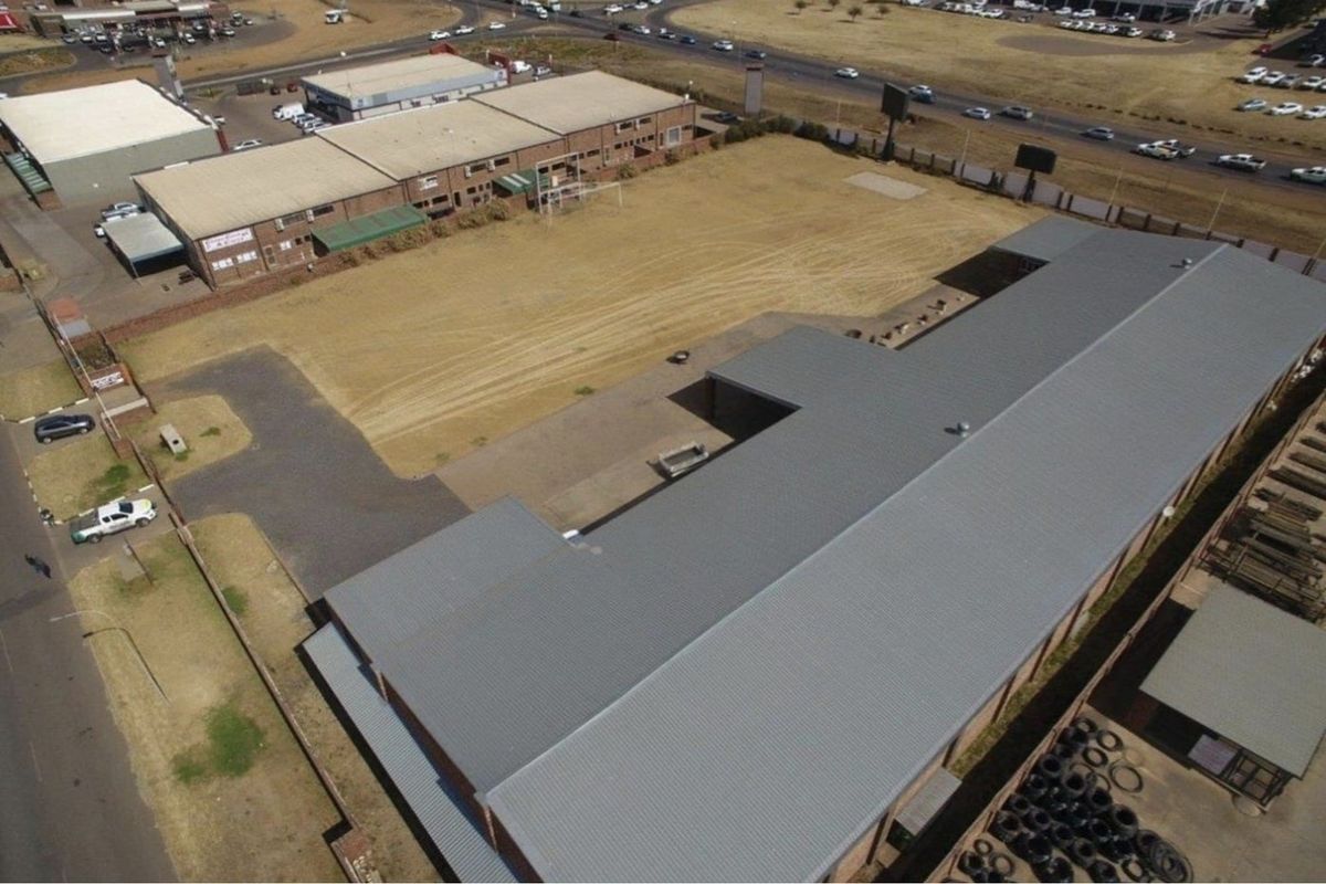 Aerial view of a commercial property featuring a large open yard, paved driveway, and a building with a metal roof.