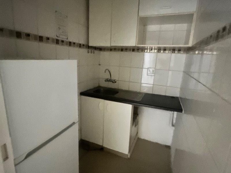 A compact scullery area featuring built-in white cabinetry, a laminate countertop, and a stainless steel sink with tiled wall finishes.