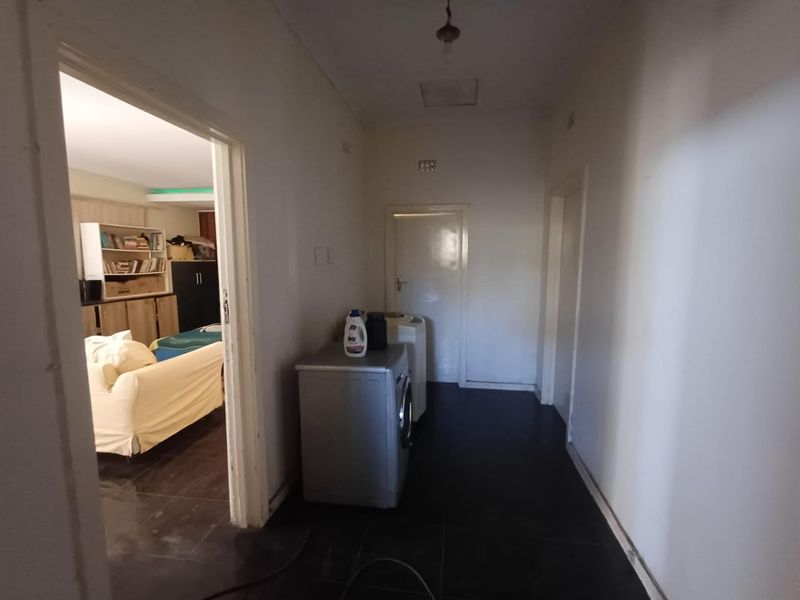 A functional hallway area featuring dark tiled flooring and access to adjacent rooms, currently used for laundry appliance placement.