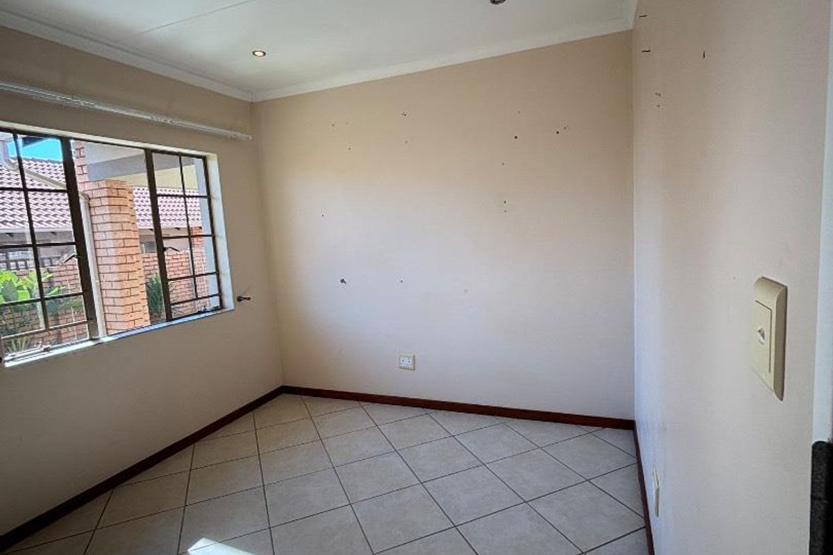 A vacant bedroom featuring tiled flooring, recessed ceiling lighting, and a window with security bars.