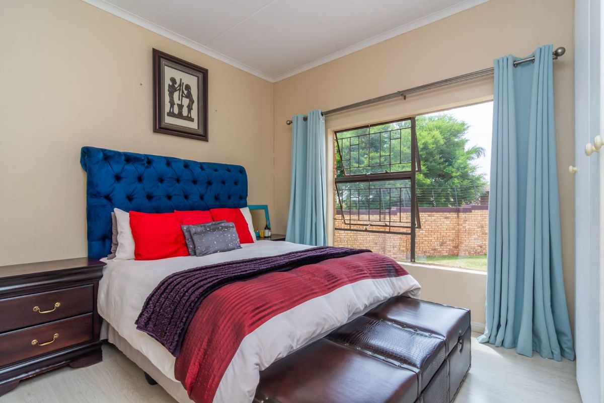 A well-lit bedroom featuring light-toned flooring, a large window with security bars, and neutral wall finishes.