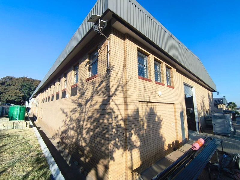 Exterior view of an industrial warehouse building featuring face brick construction, metal roofing, and a large roller shutter door for vehicle access.