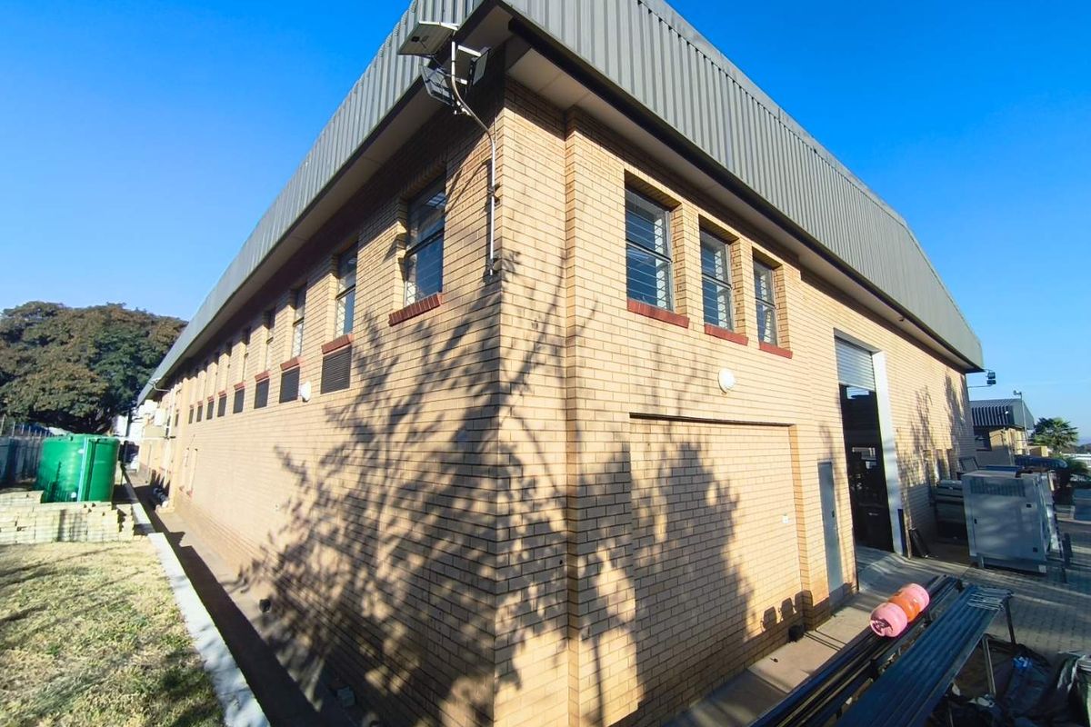 Exterior view of an industrial warehouse building featuring face brick construction, metal roofing, and a large roller shutter door for vehicle access.
