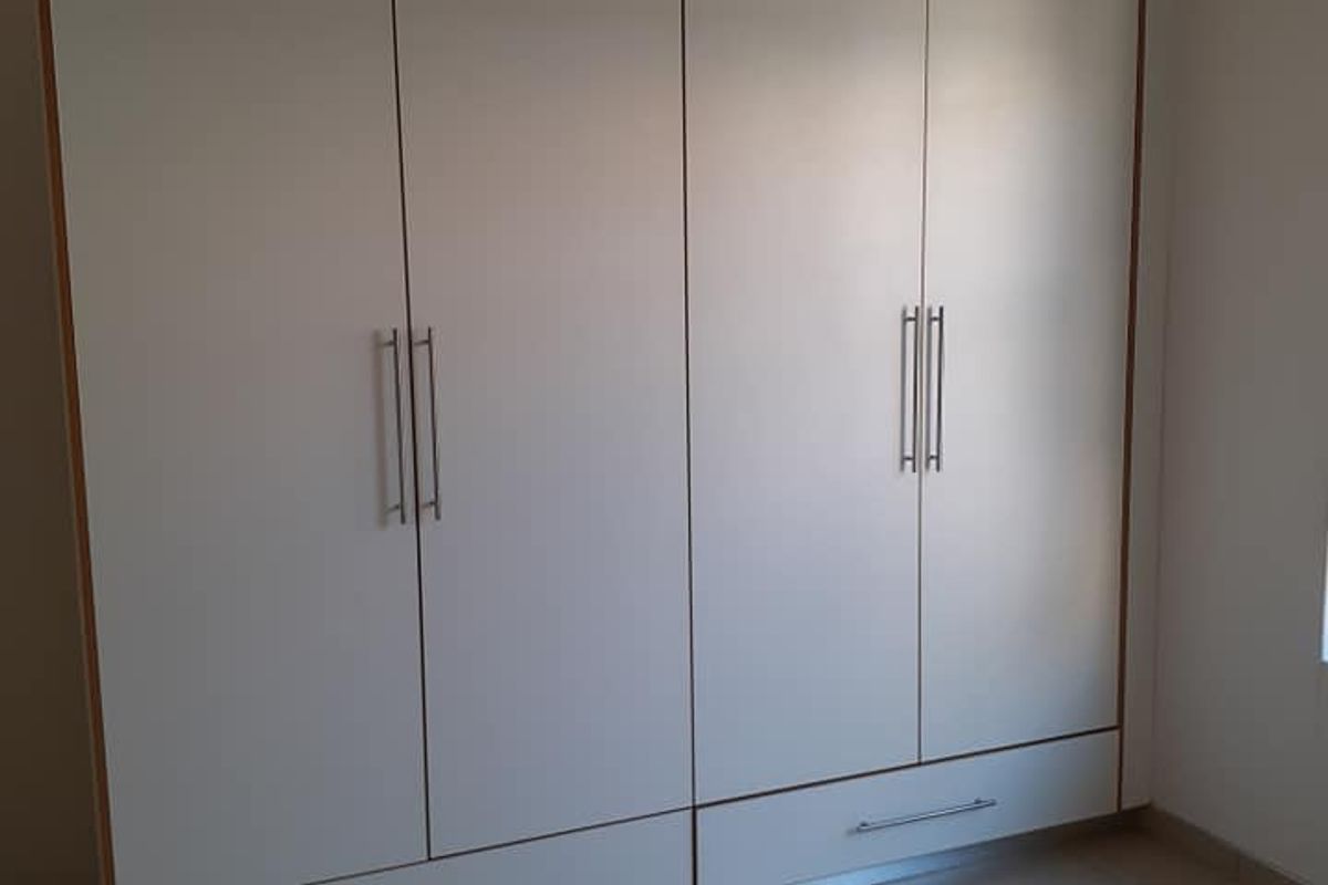 A bedroom featuring built-in floor-to-ceiling wardrobes with modern handles and neutral tiled flooring.