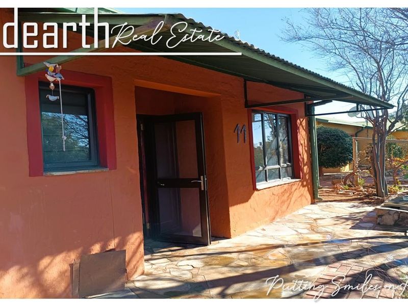 Front entrance of a retirement unit featuring a covered patio with stone paving and a security screen door.