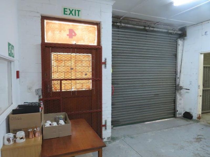 Industrial garage space featuring a large roller shutter door, security gate, and functional lighting, suitable for storage or workshop use.