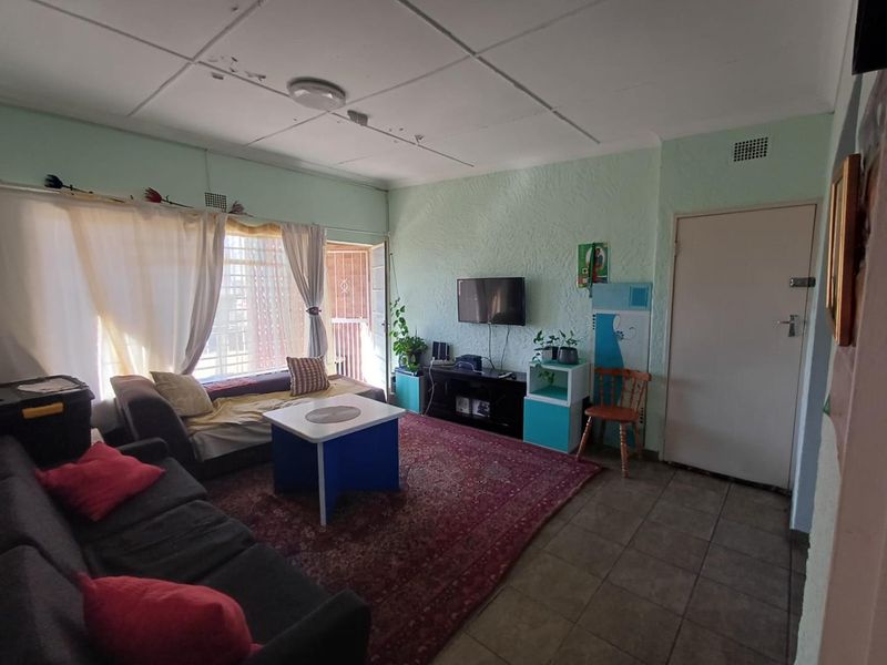 A living room featuring tiled flooring, textured walls, and a ceiling with visible wear, providing access to an exterior area via a security gate.