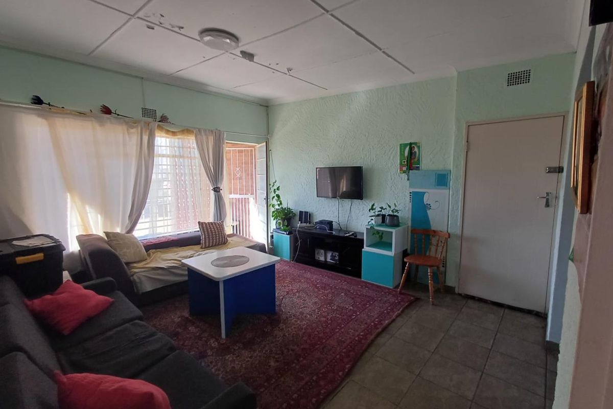 A living room featuring tiled flooring, textured walls, and a ceiling with visible wear, providing access to an exterior area via a security gate.