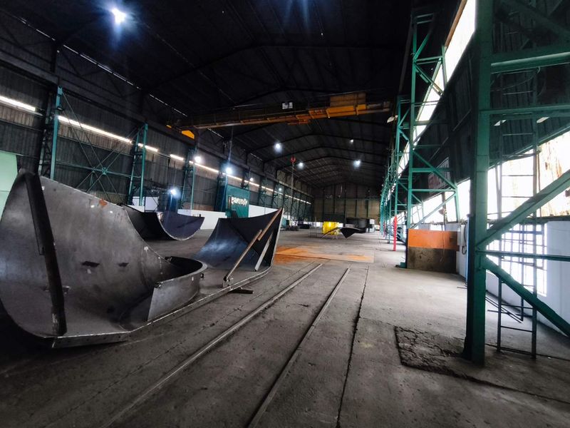 Spacious industrial warehouse featuring high ceilings, overhead crane infrastructure, and durable concrete flooring, suitable for manufacturing or storage operations.