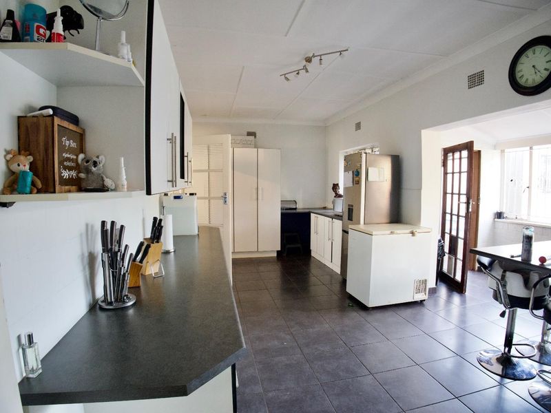 A functional kitchen featuring dark tiled flooring, ample built-in cabinetry, laminate countertops, and direct access to an outdoor area through a glass-paned door.