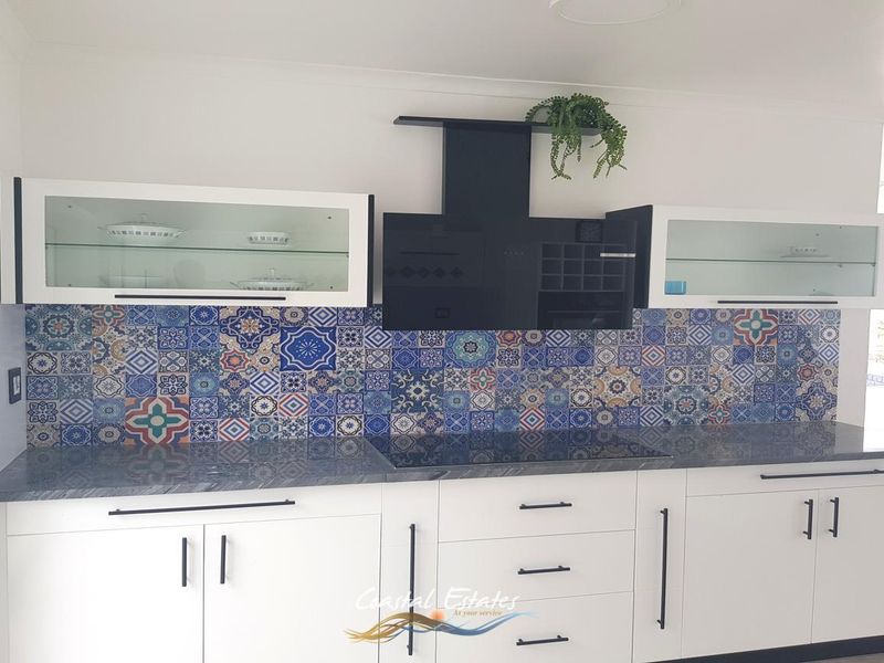 Modern kitchen featuring white cabinetry, a striking patterned tile backsplash, dark stone countertops, and a built-in induction hob with a black extractor fan.