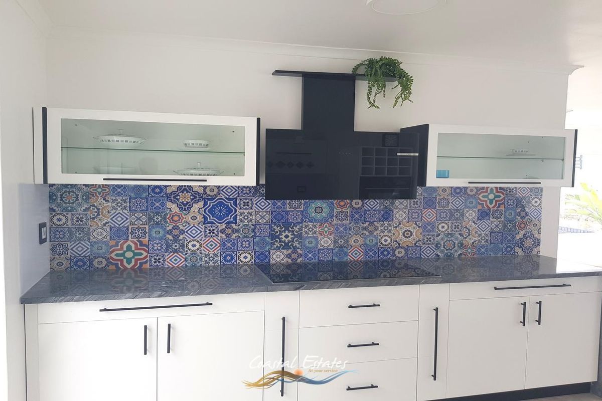 Modern kitchen featuring white cabinetry, a striking patterned tile backsplash, dark stone countertops, and a built-in induction hob with a black extractor fan.