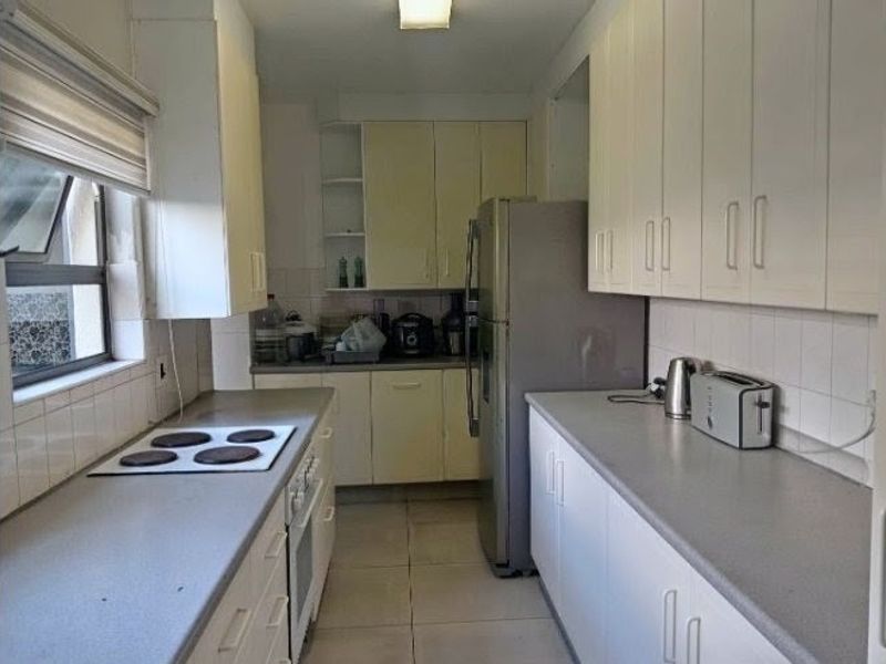 Functional galley-style kitchen featuring ample built-in cabinetry, laminate countertops, electric hob, and tiled finishes throughout.