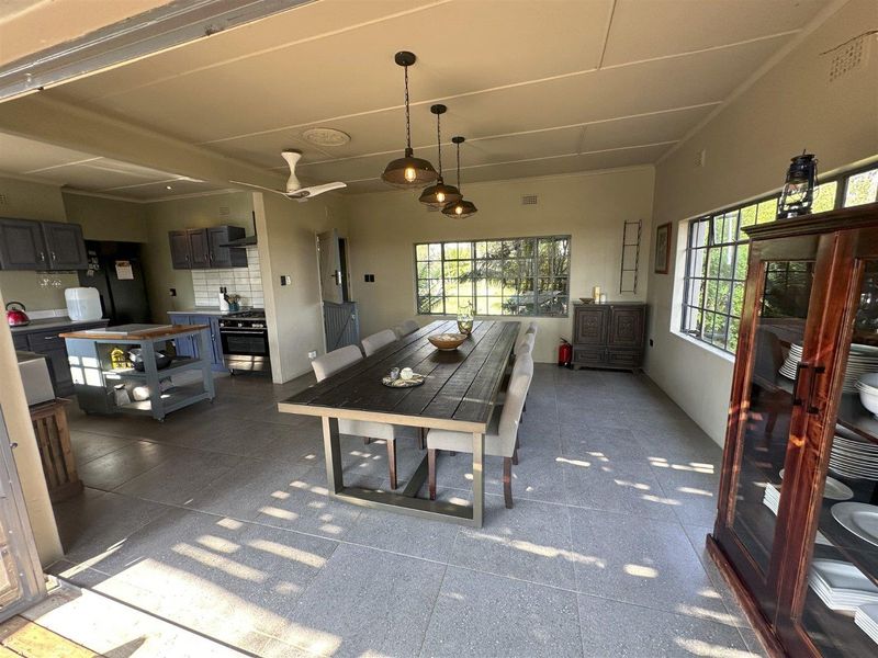 Spacious open-plan living and dining area featuring a modern kitchen with dark cabinetry, tiled floors, and large steel-framed windows providing natural light.
