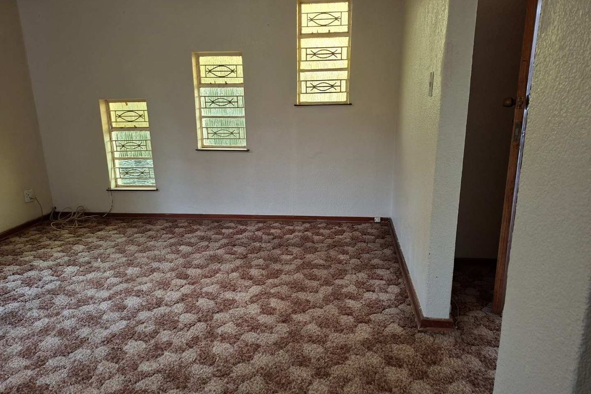 A vacant bedroom featuring textured brown carpeting and three windows fitted with security bars, offering a blank canvas for renovation.