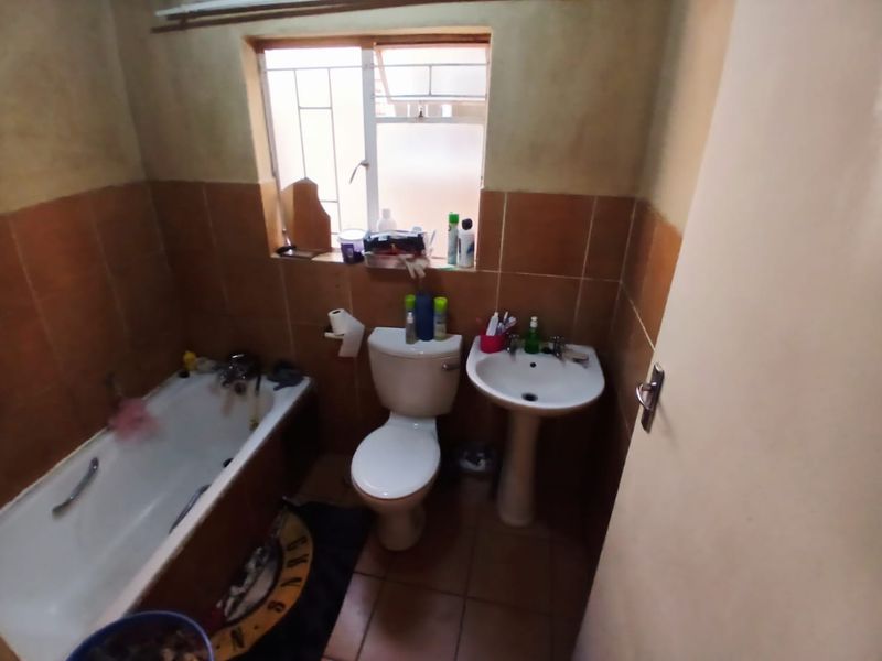 A compact bathroom featuring a bathtub, pedestal basin, and toilet with dated wall tiling and a window with security bars.