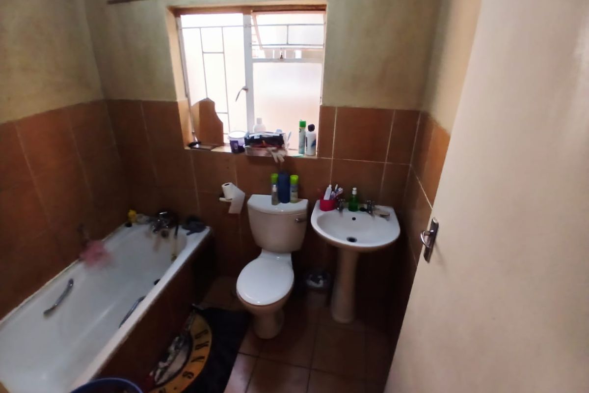 A compact bathroom featuring a bathtub, pedestal basin, and toilet with dated wall tiling and a window with security bars.