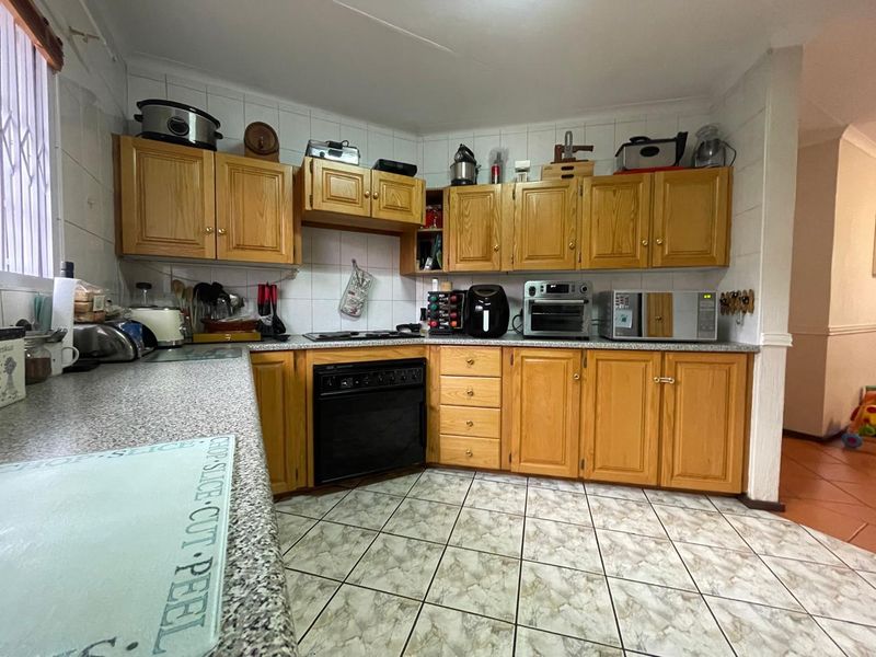 A functional kitchen featuring traditional wooden cabinetry, laminate countertops, tiled backsplash, and ceramic floor tiles, providing ample storage and workspace.