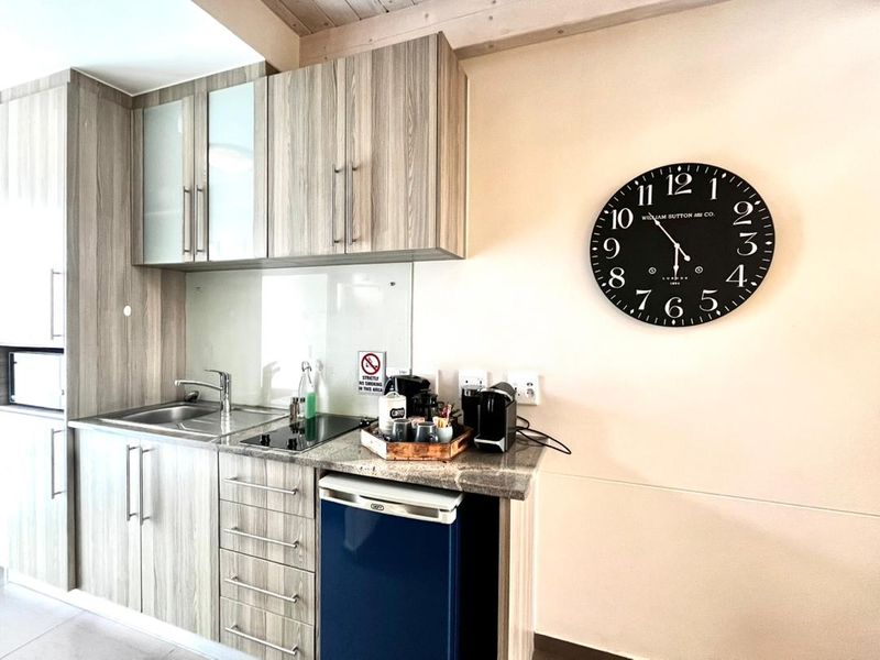 A compact, modern kitchenette featuring wood-grain cabinetry, granite countertops, a stainless steel sink, and a built-in electric hob.
