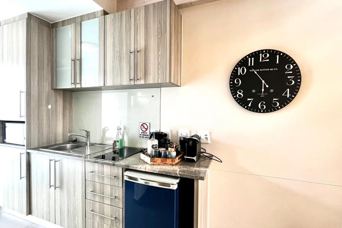 A compact, modern kitchenette featuring wood-grain cabinetry, granite countertops, a stainless steel sink, and a built-in electric hob.