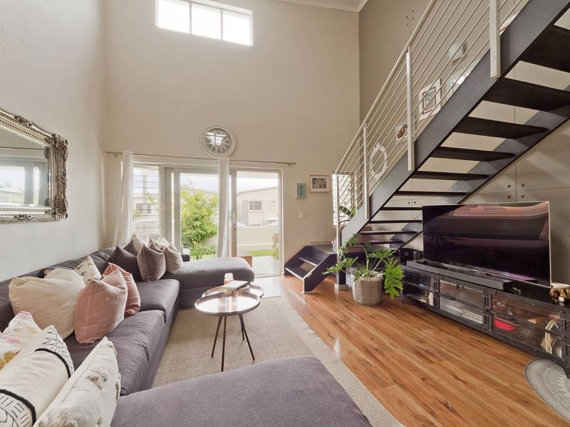 Spacious double-volume living area featuring hardwood flooring, a modern metal staircase, and large sliding doors providing access to the outdoor space.