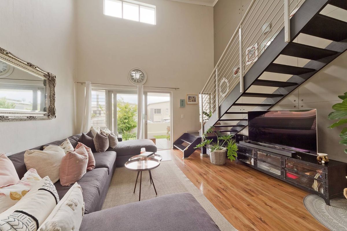 Spacious double-volume living area featuring hardwood flooring, a modern metal staircase, and large sliding doors providing access to the outdoor space.