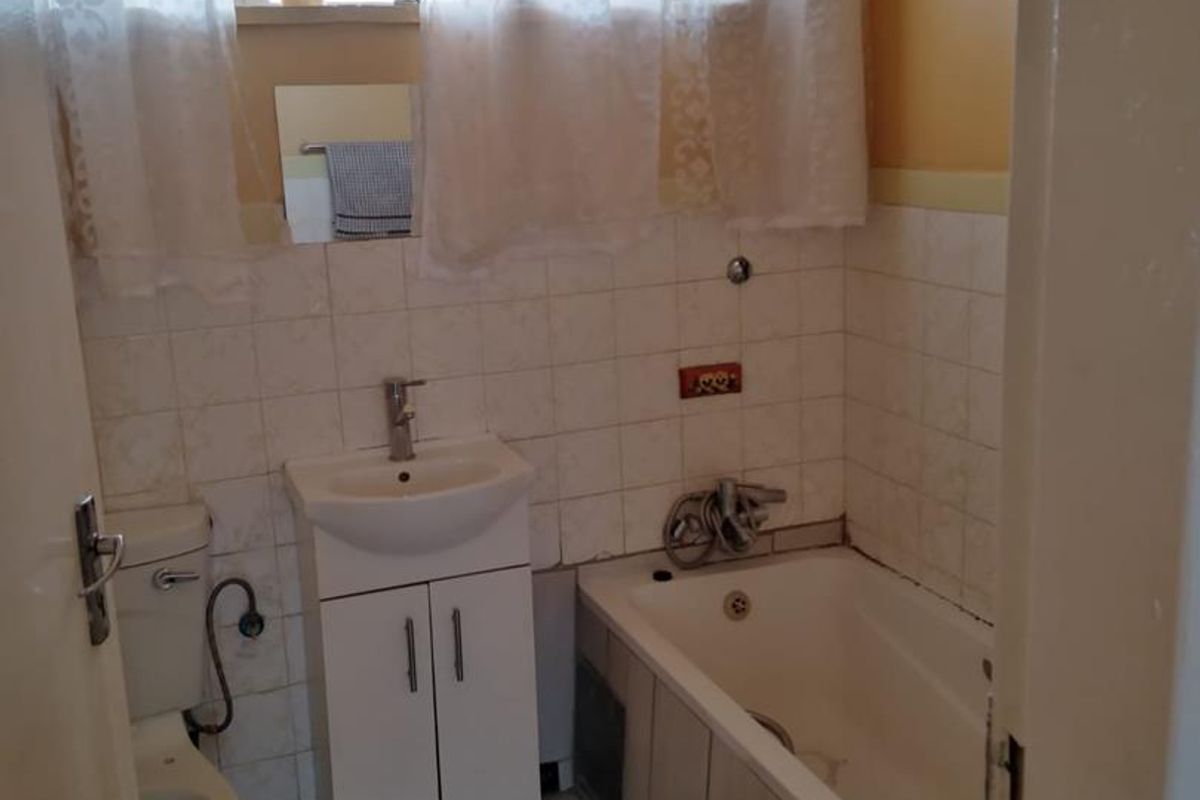 A functional bathroom featuring a built-in bathtub, vanity basin, and toilet with tiled walls and flooring.
