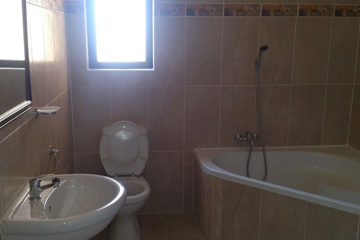 A functional bathroom featuring a corner bathtub with handheld shower, pedestal washbasin, toilet, and neutral wall tiling with a decorative border.