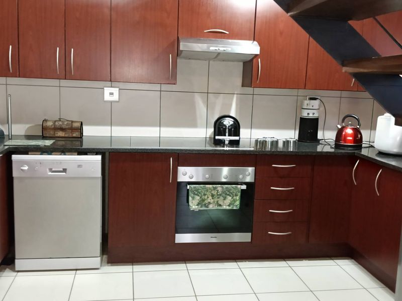 A functional kitchen featuring dark wood cabinetry, granite countertops, stainless steel oven, and extractor fan, with tiled flooring and an adjacent staircase.