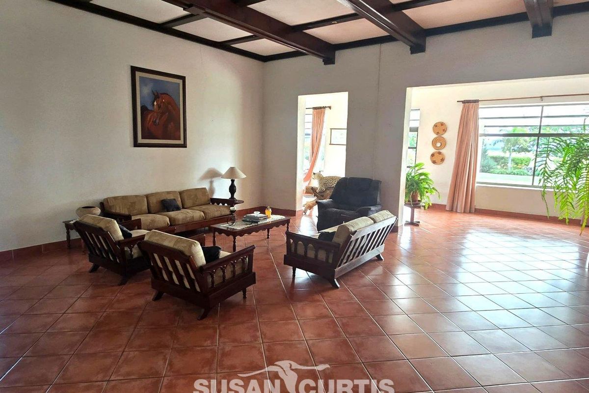 Spacious living area featuring exposed timber ceiling beams and terracotta floor tiles, offering a bright and open layout with large windows.