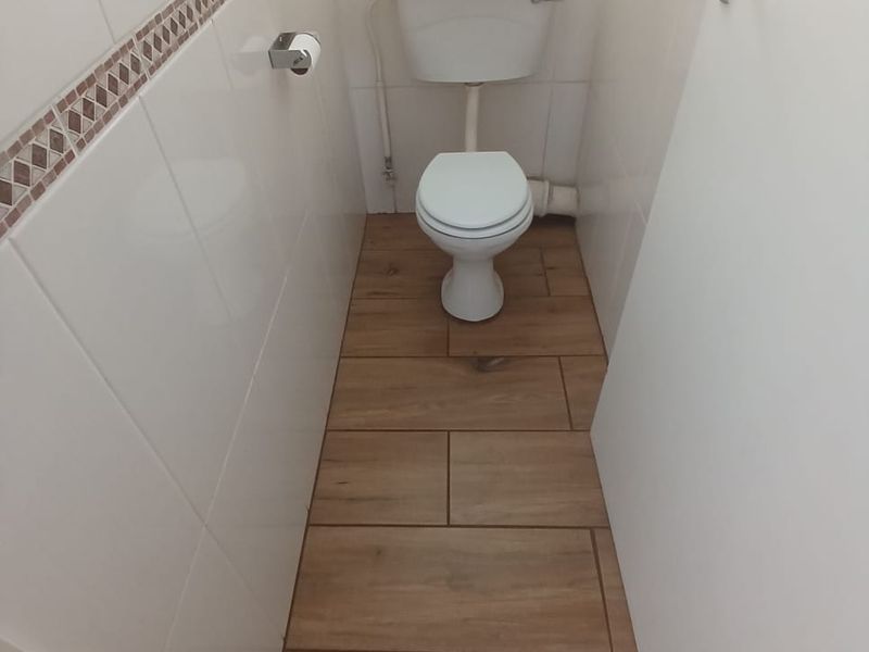 A compact, clean guest toilet featuring modern wood-look floor tiles and white wall tiles with a decorative border.
