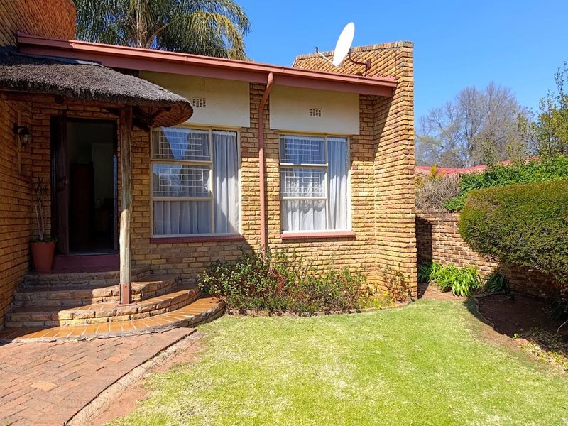 Rear view of a face brick cottage featuring a small thatched porch, paved walkway, and a well-maintained garden area.