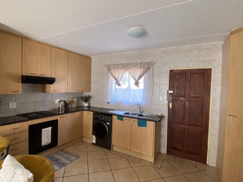 Functional kitchen featuring light wood cabinetry, tiled backsplash, built-in oven with hob, and integrated laundry appliance space with direct exterior access.