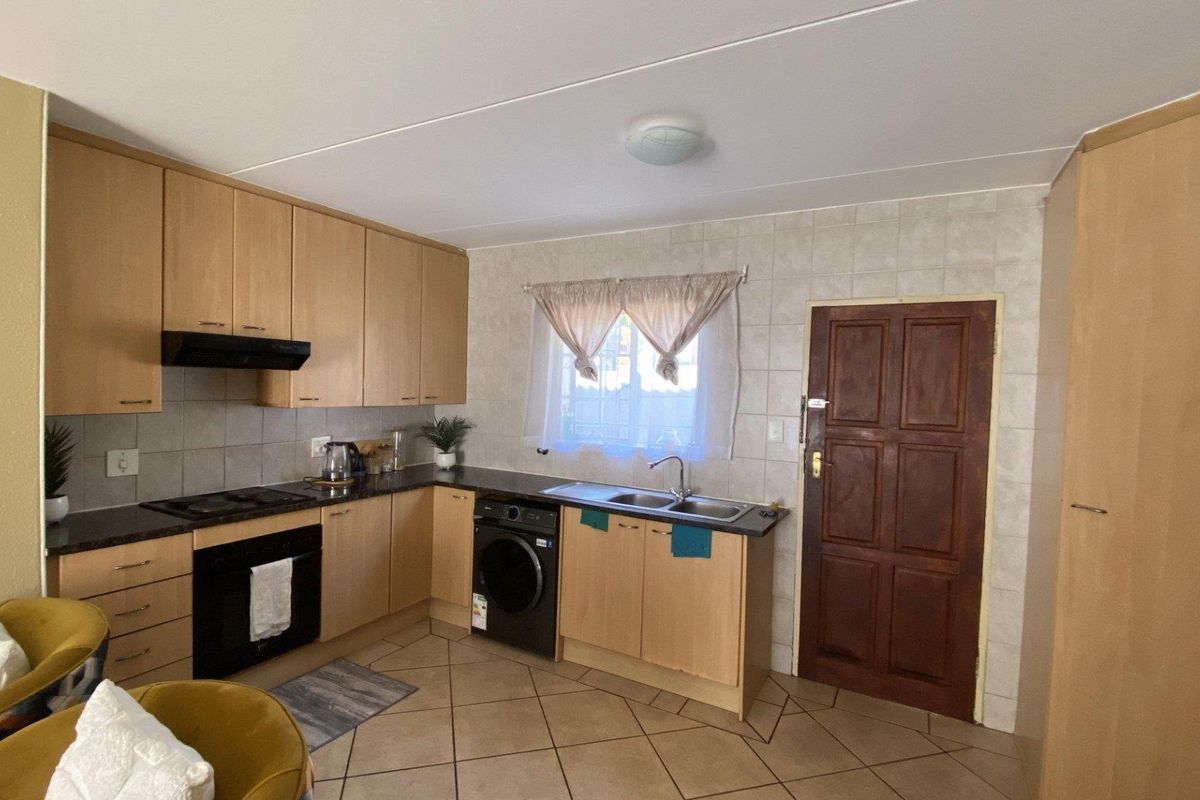 Functional kitchen featuring light wood cabinetry, tiled backsplash, built-in oven with hob, and integrated laundry appliance space with direct exterior access.