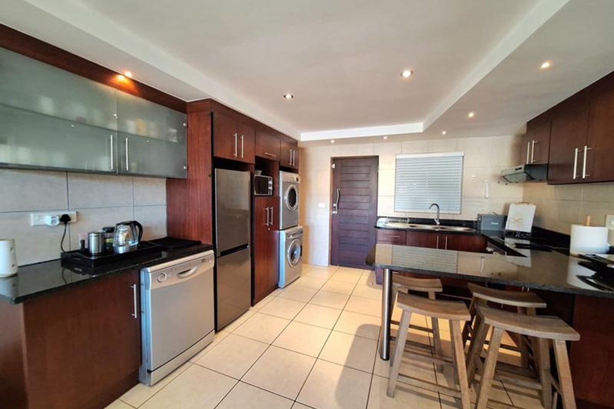 Modern kitchen featuring dark wood cabinetry, granite countertops, integrated appliances, and a breakfast bar, with tiled flooring and recessed lighting throughout.