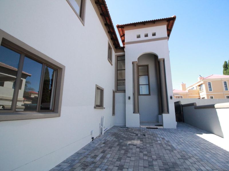 A view of the rear exterior featuring a paved courtyard, arched architectural detailing, and a well-maintained facade with terracotta roof tiles.