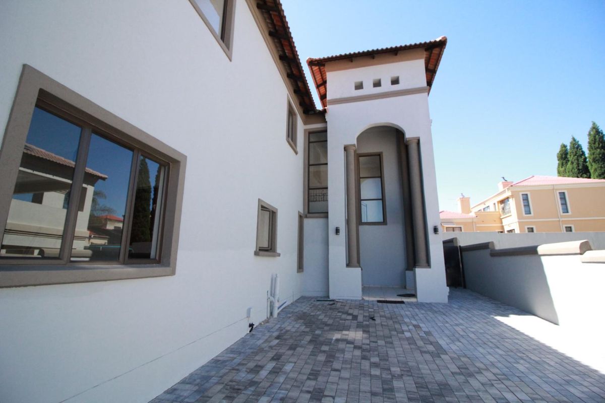 A view of the rear exterior featuring a paved courtyard, arched architectural detailing, and a well-maintained facade with terracotta roof tiles.