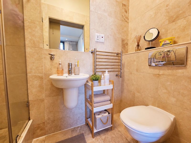 Modern bathroom featuring a wall-mounted basin, wall-hung toilet with concealed cistern, heated towel rail, and a glass-enclosed shower with neutral floor-to-ceiling tiling.