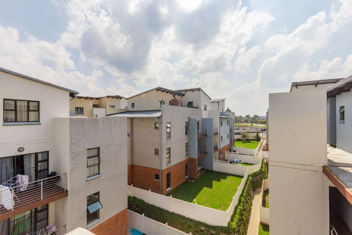 An elevated view of the apartment complex rear exterior, featuring landscaped lawns, paved walkways, and private balconies with metal railings.