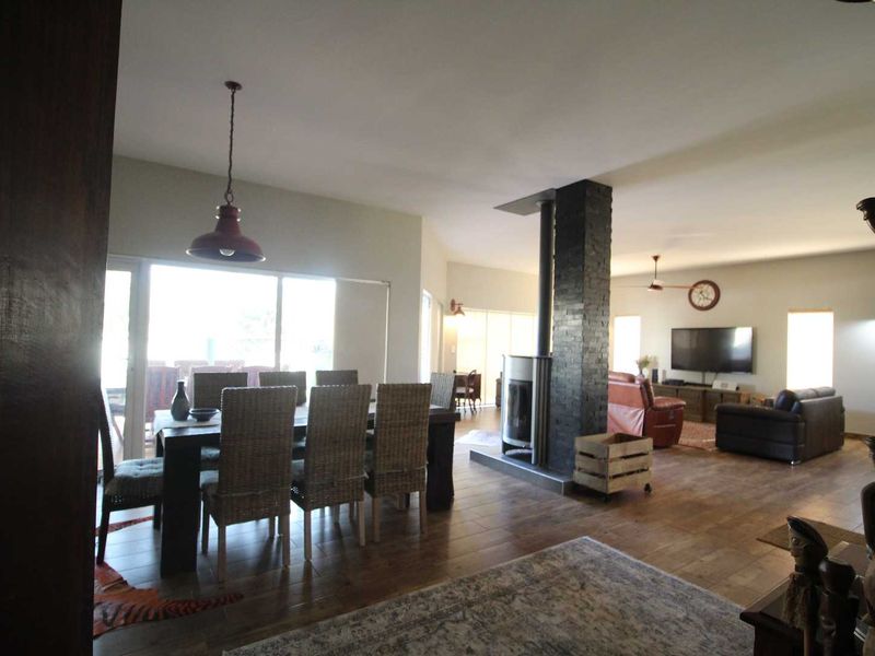 Spacious open-plan living and dining area featuring hardwood flooring, a central stone-clad wood-burning fireplace, and large sliding glass doors leading to the outdoors.