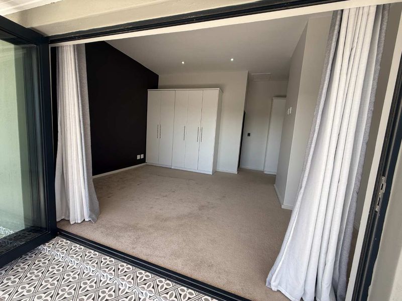 Spacious bedroom featuring built-in cupboards, neutral carpeting, and large bi-fold doors opening to an outdoor area.