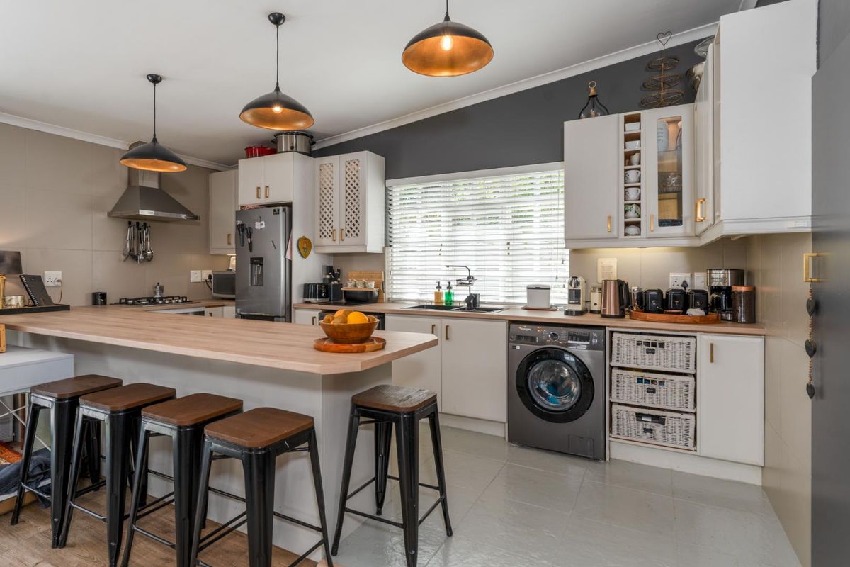 A functional kitchen featuring white cabinetry, light wood-look countertops, a breakfast bar, integrated washing machine, and modern pendant lighting.