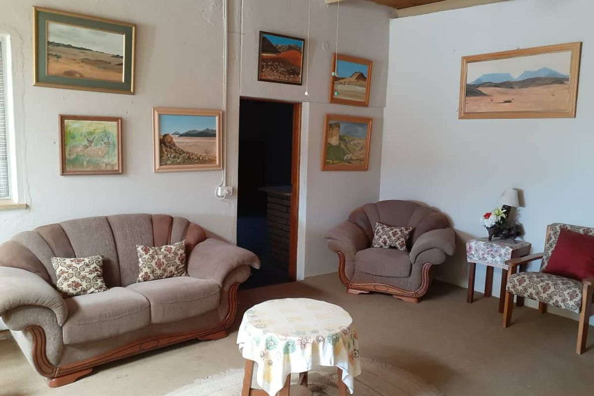 A living room featuring exposed timber ceiling beams, carpeted flooring, and wall-mounted artwork, providing a dated but functional living space.